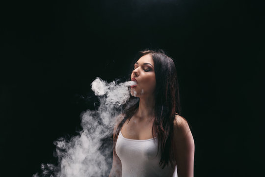 Young woman vaping e-cigarette with smoke on black