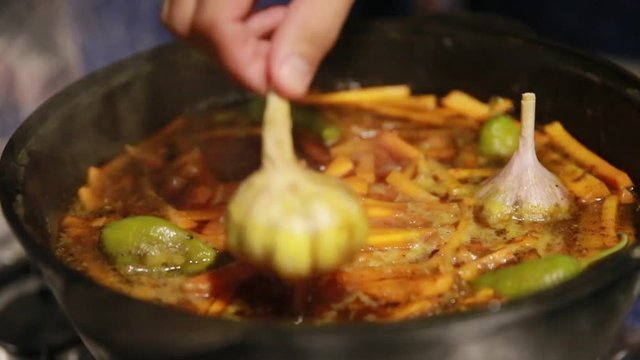Cooking pilaf, shef removes garlic and green chili peppers from cast-iron kettle