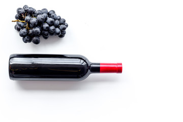 Bottle of red wine near bunch of grapes on white background top view copyspace