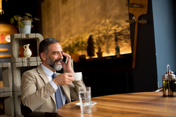 Middle-aged businessman drinking coffee and uses mobile phone incafe