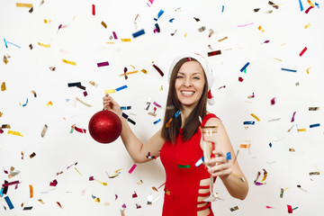 Fototapeta premium Beautiful smiling caucasian young happy woman in red dress and Christmas hat standing with big tree toy and glass of champagne on white background confetti. Santa girl isolated. New Year 2018 holiday