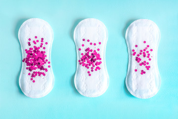 Menstrual pad with bright purple glitter on blue colored background. Woman periods cycle, menstruation frequency. Minimalist still life photography concept
