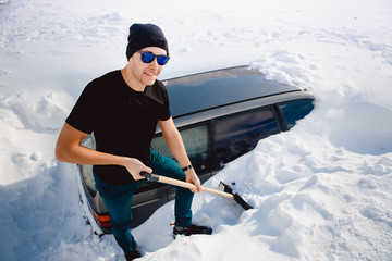 Man cleans snow and cleans car shovel from snow, strong blizzard and hurricane.