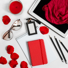 Obraz na płótnie Canvas Notepad, pen, tablet, candle, stationery on white background with red flower petals, concept of female fashionable workplace