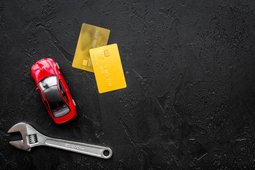 Pay for car repair. Wrench near car toys and bank card on black background top view copyspace