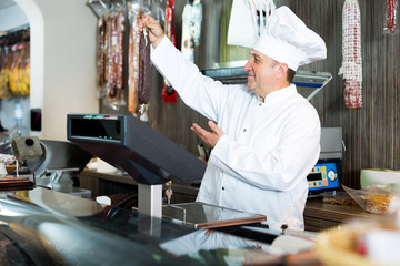 Male seller posing with wursts in butchery