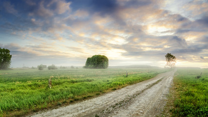 Fototapeta premium грунтовая дорога в сельском поле с туманом, летом на закате дня, Россия, Урал