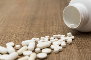 Heap of white capsules on wooden table.