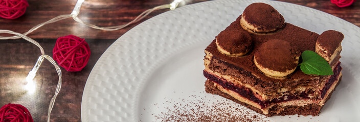 Panoramic photo of a tiramisu with fresh mint on a white plate with cinnamon, lights and red Christmas balls
