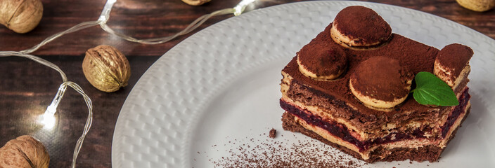 Panoramic photo of a tiramisu with fresh mint on a white plate with cinnamon, lights and red Christmas walnuts