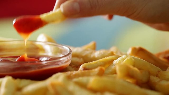 Eating french fries - hand taking a piece dipping it in ketchup, macro closeup