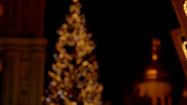 Blured christmas tree with flashlights. Churches in the background.