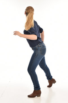 Full length portrait of a girl wearing simple blue shirt and jeans, standing pose facing away on a white background.