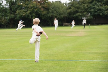 young player warms up by stretching in preparation for game of school cricket on English village green 