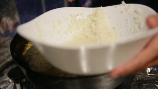 Cooking pilaf, shef adds white rice into cast-iron kettle and move it with spoon