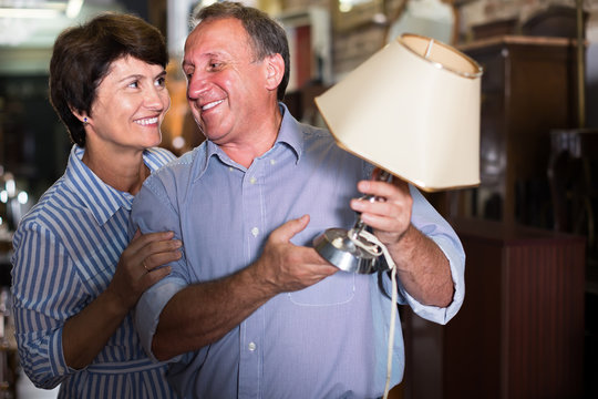 Nice Mature Couple Is Shopping The Old Lamp In The Antique Store