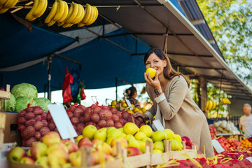 Woman in a market at the shelf for fruits shopping for groceries, she is checking out the apples.