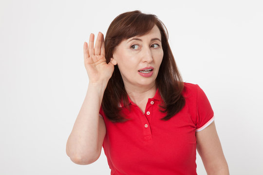 Summer Gossip concept. Portrait of pretty middle aged woman with palm near her ear. Red blank polo shirt. Copy space