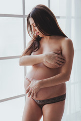 Beautiful pregnant woman naked, standing near white light window