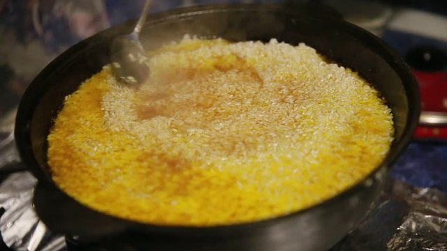 Cooking pilaf, shef distributes evenly white rice in the cast-iron kettle