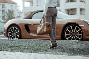 Cool man beautiful model outdoors, city style fashion. A handsome man model walking in the city center next to some cars. urban setting. The young boy as trendy, modern clothing with bag
