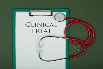 Medecine concept - clipboard with text "Clinical trial" and red stethoscope on green paper background