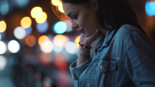 Attractive young woman in jeans jacket enjoying the moment, posing to camera. night city lights on the background. Joy of life, active lifestyle. Slow motion, camera stabilizer shot, female portrait