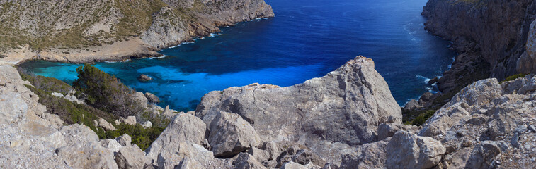 A panoramic picture of clear bright blue waters surrounded with rocky mountainous landscape