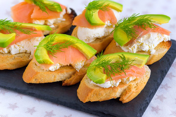 Bruschetta, snack sandwiches with white cheese, smoked salmon and pieces of avocado decorated by dill.