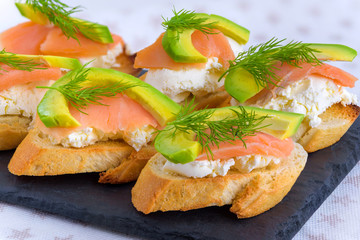 Bruschetta, snack sandwiches with white cheese, smoked salmon and pieces of avocado decorated by dill.