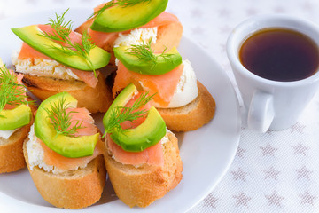 Bruschetta, snack sandwiches with white cheese, smoked salmon and pieces of avocado decorated by dill.
