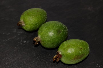 Green fresh exotic fruits feijoa on a black background made from natural slate stone.