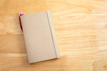 Blank brown notebook with pen on wood background