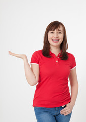 Smiling beautiful woman wearing blank red t-shirt and blue jeans and showing something by her finger, mock up on white background.