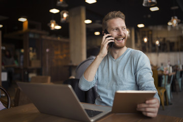Obraz na płótnie Canvas Young happy man having phone call in cafe