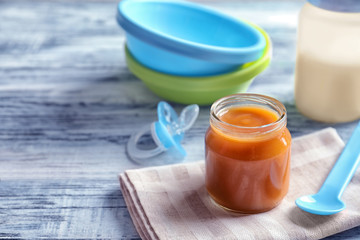 Jar and spoon with healthy baby food on wooden table
