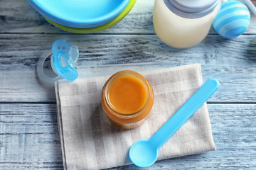 Jar and spoon with healthy baby food on wooden table