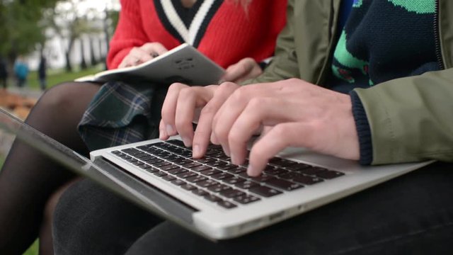 Guy and Girl Students with Laptop on Bench in Park write notes, read a Textbook