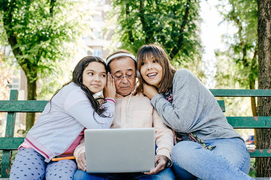 .A father with his daughters sitting on a stone bench, learning to use the laptop. Relaxed autumn day in family outdoors. Lifestyle portrait...