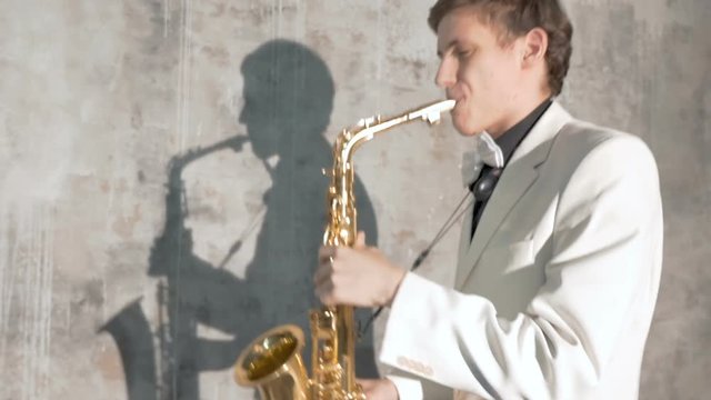 A musician in a white suit plays the saxophone. He performs in a nightclub, against a gray background. close-up
