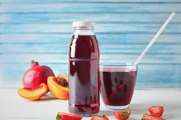 Bottle and glass with fruit juice on table against light wall
