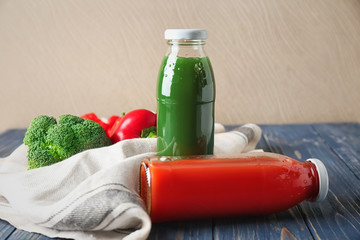 Bottles of fresh vegetable juices on table against light wall