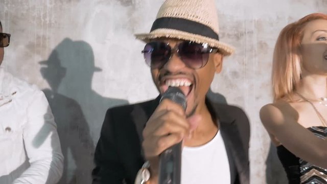 An African male singer sings an emotional song. He acts in company with other musicians. Close-up.