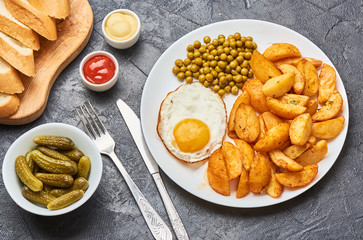 Fried potatoes with fried eggs, green peas on concrete gray background