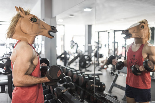 Horse face man training lifting weights in gym looking his reflection in mirror