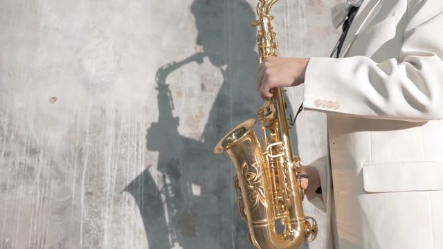 A musician in a white suit plays the saxophone. He performs in a nightclub, against a gray background. close-up