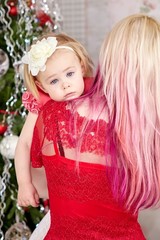 Young mother with a tired baby girl in front of xmas tree. Christmas family portrait.