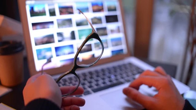 Young Man with Glasses work with Laptop, browse Photos in internet