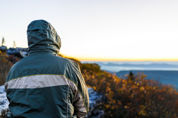 Standing young man in green coat jacket with hood on windy cold autumn morning in Bear Rocks, West Virginia looking at sunrise