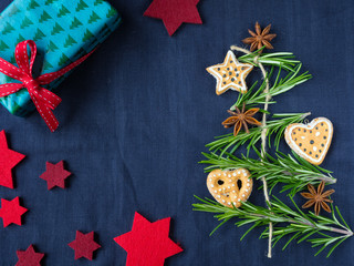 Christmas tree made from rosemary, anise star and gingerbread cookies.  Christmas box with red ribbon and stars on blue background.